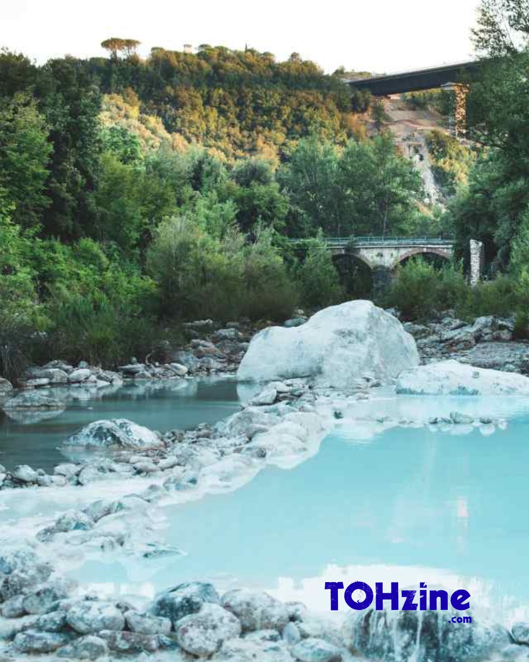 Bagni di Petriolo, vasche di acqua termale azzurra nel fiume Farma con ponte e bosco sullo sfondo